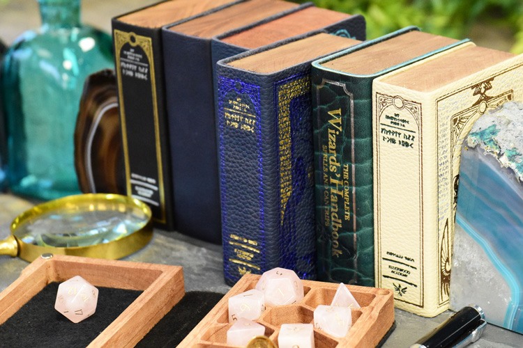 A row of mini spellbook gaming boxes on a slate shelf with rose quartz dice