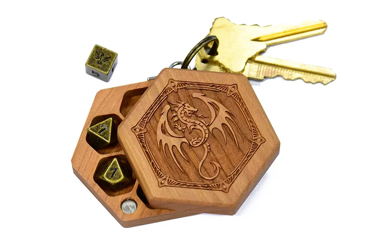 A cherry wood Mini Hex Chest dice box with a winged dragon engraving and gold metal mini polyhedral dice for tabletop gaming
