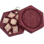A purpleheart wood Mini Hex Chest dice box with a Celtic knot engraving and pink rose quartz mini polyhedral dice for tabletop gaming